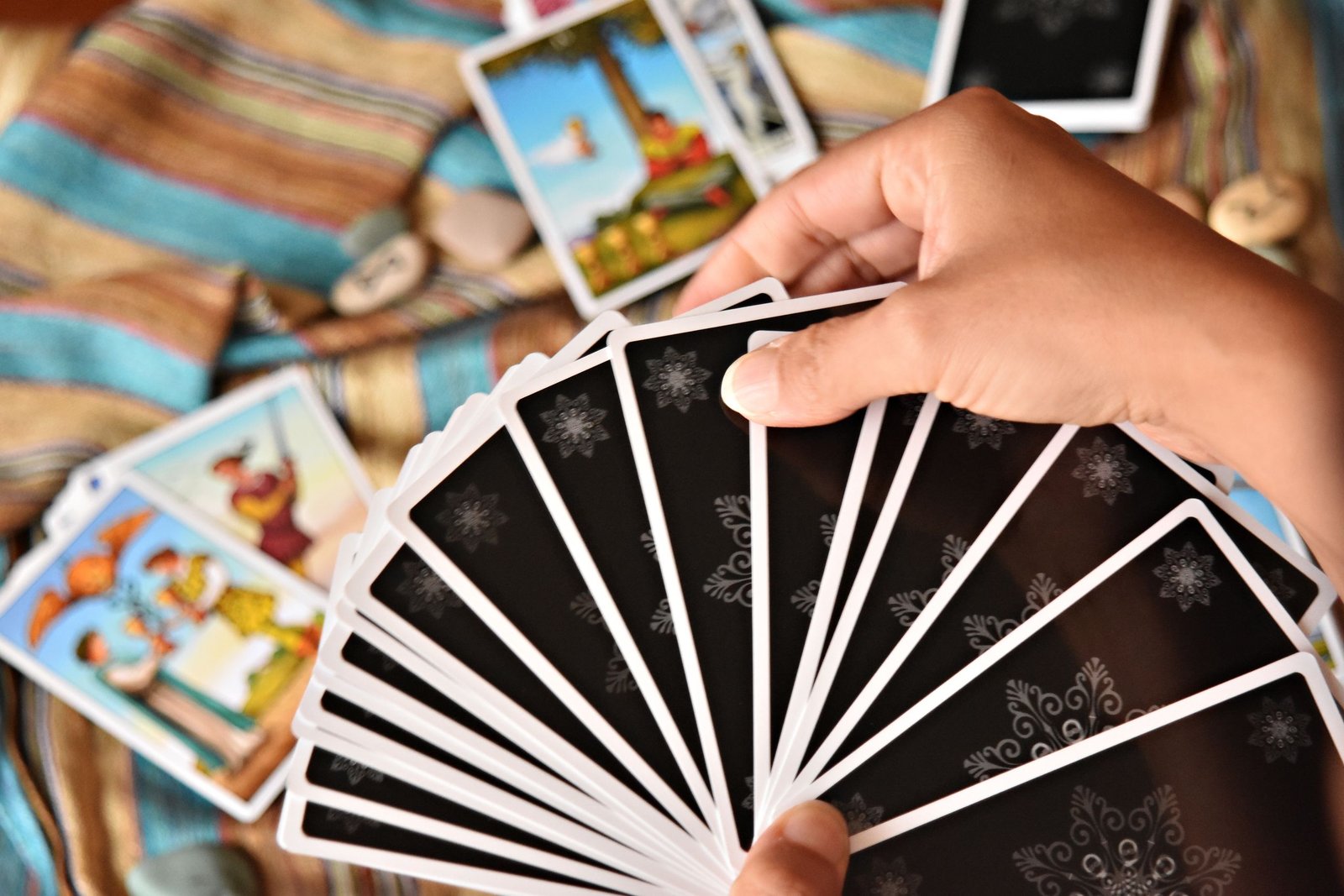 A hand holding a fanned set of tarot cards over a colorful tapestry.