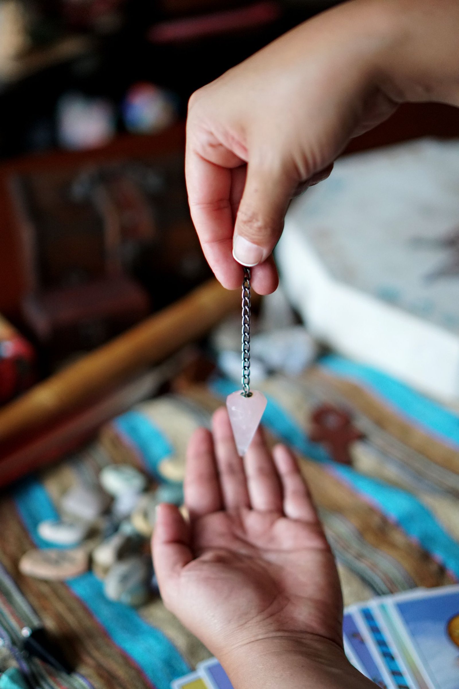 A person holding a rose quartz pendulum over an open hand, indicating divination or energy practice.