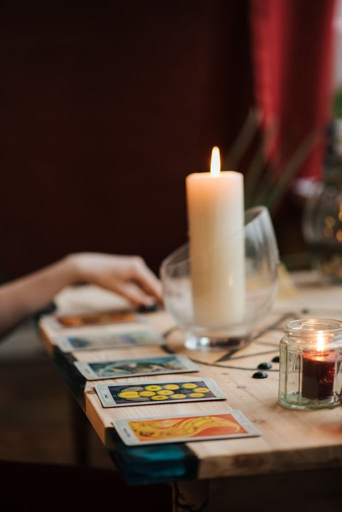 Crop unrecognizable fortune teller with tarot cards near burning wax candles during divination process at home